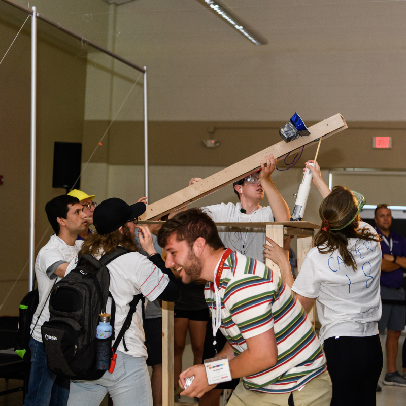 A team loads their catapult to launch objects over a wall for their rover to collect. 