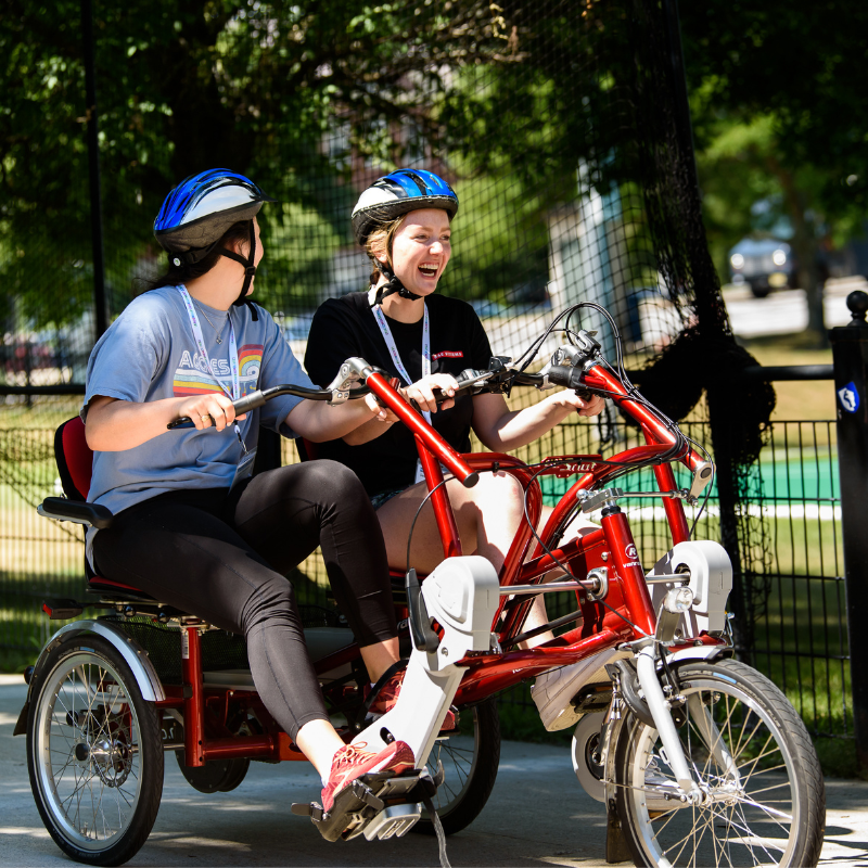 Two BAE Systems Leadership Development Program members riding a tandem bicycle during a team building activity.