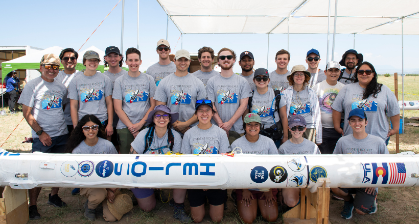 A group of interns posing for a photo as they build a model projectile as part of the BAE Systems Intern Remote Sensing team.