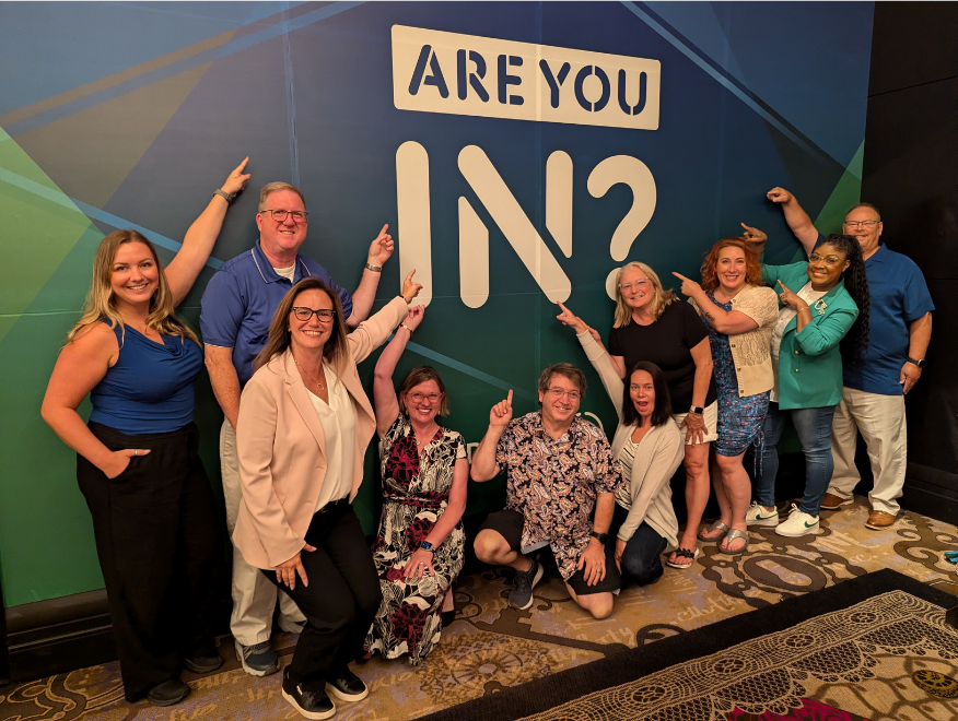 A group of BAE Systems employees pointing at the "Are you In?" logo at the Disability:IN national conference.