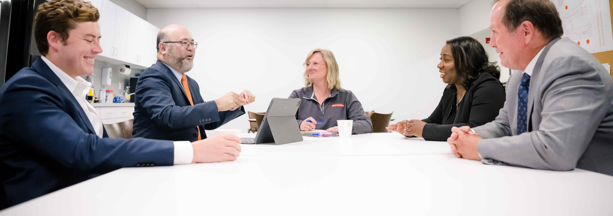 Five BAE Systems employees gather around the break room table.