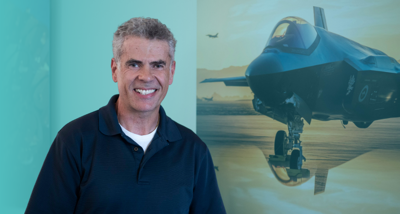 Team member poses for a photo in front of a picture featuring a jet.