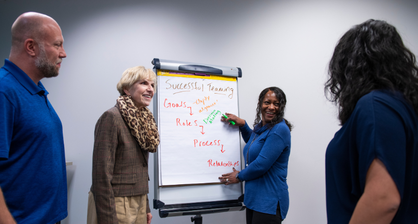 Four employees working on a large notepad during a brainstorm. 