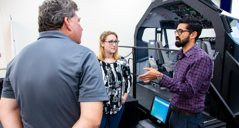 Three BAE Systems employees talking to each other in front of a flight deck control model. 