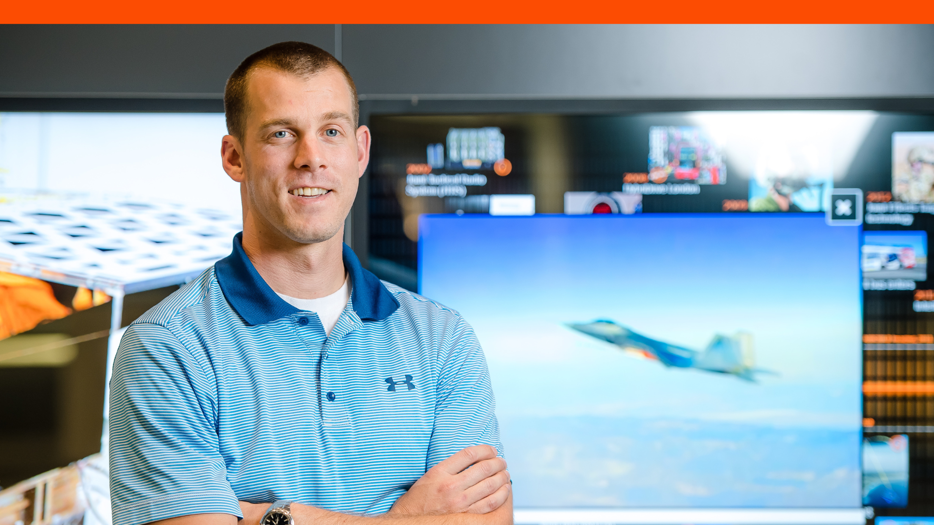Nick, a systems engineer at BAE Systems, smiles for a headshot in front of a screen displaying an aircraft.