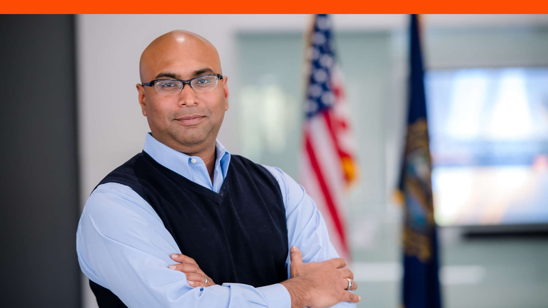 Sayed, an engineer at BAE Systems smiles for a photo in front of the American flag.