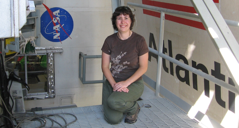 A BAE Systems employee in the Space & Mission Systems sector kneels beside Space Shuttle Atlantis, surrounded by aerospace equipment and mission support infrastructure. The image highlights hands-on expertise, innovation, and the engineering talent that helps advance space missions and national security.