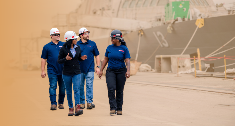 Four BAE Systems ship repair employees walking and talking at the ship yard.