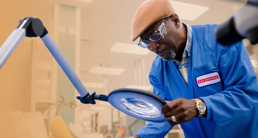 Elmer, a electronic test technician uses a magnyfying glass to look at a curcuit board.