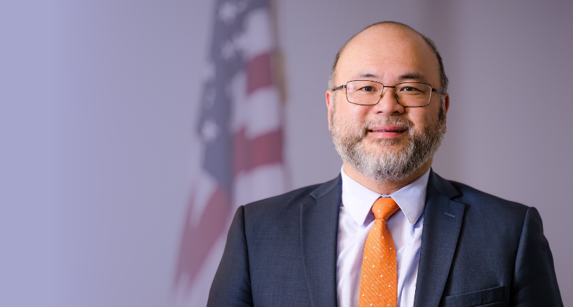 Howard, a wargaming analyst, poses for a professional headshot in front of an American flag.