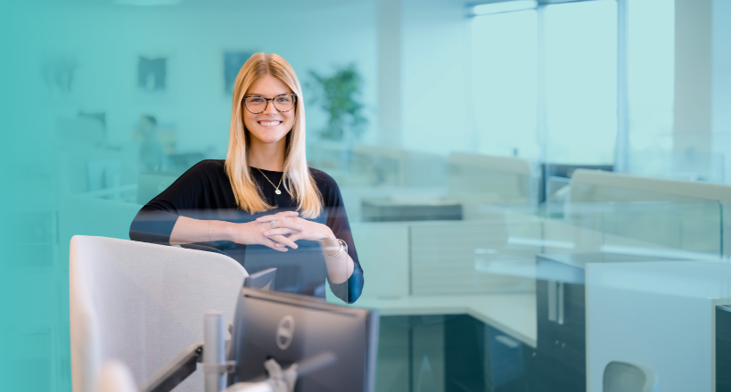 Olivia, a talent operations specialist, smiles for a photo in her cubicle located at Inc. Headquarters in Falls Church.