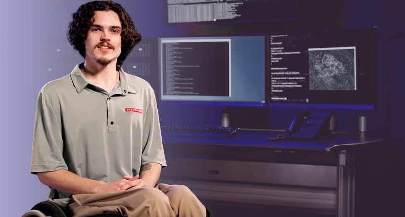 Individual sitting in a wheelchair with computers behind him with code on them.