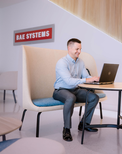 Tony, a program manager, works on his computer. A BAE Systems logo is on the wall behind him.