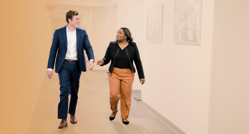 Two co-workers walking down a hallway as they converse.