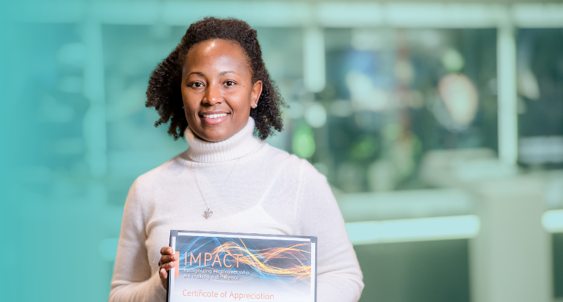 Monica, a production program manager, holds an Impact Award in her hands as she smiles for a photo.