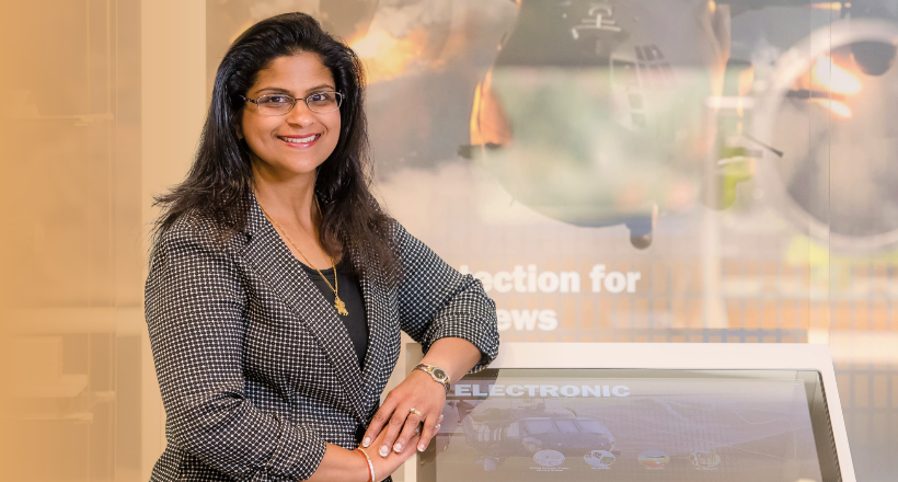 Neeta, a program director, smiles for a photo in front of a photo of a military jet.