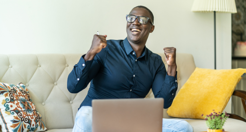 Man sitting on a couch cheering after finding out good news.