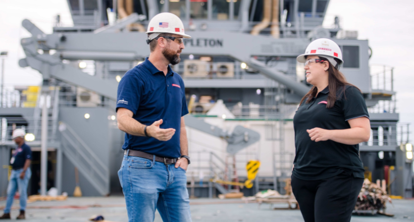 Two BAE Systems employees talk while standing on a Navy vessel.