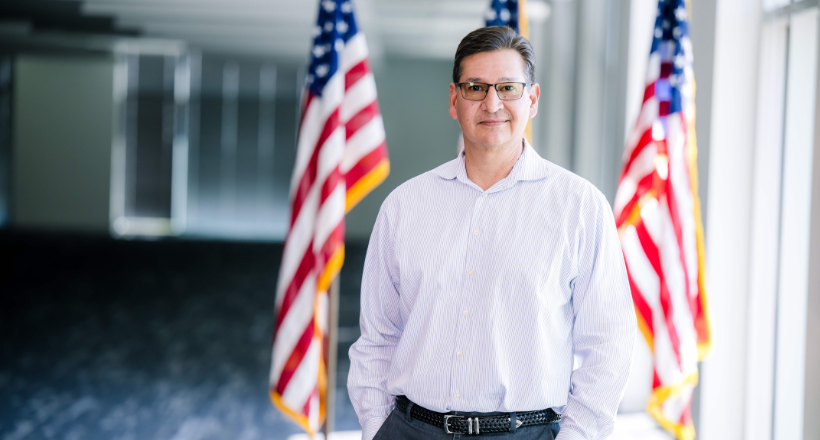 Richard, an engineering manager stands in front of the American flag for a photo.