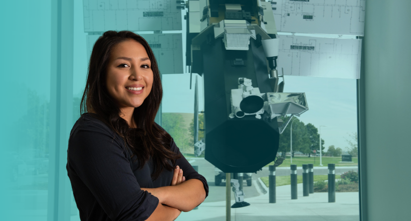 Space and Mission Systems employee smiles in front a model satallite. 