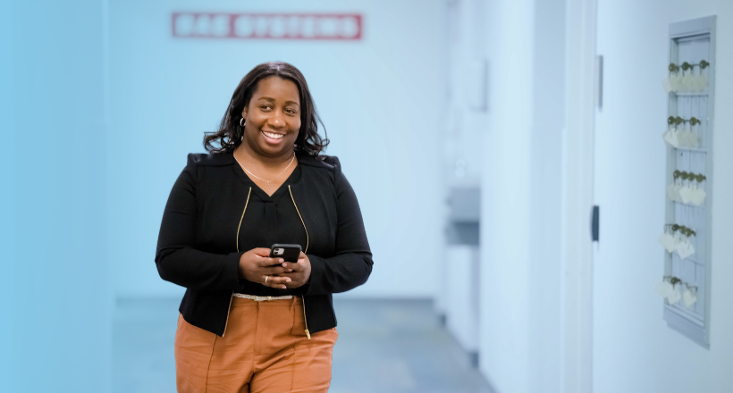 Ronda, a BAE Systems program manager smiles as she walks down the hallway holding her phone.