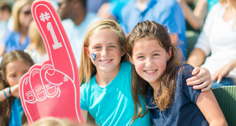 Two young girls posing for a photo at a local sports event. 