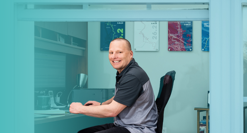 Remote employee smiles for a photo while sitting at his home desk.