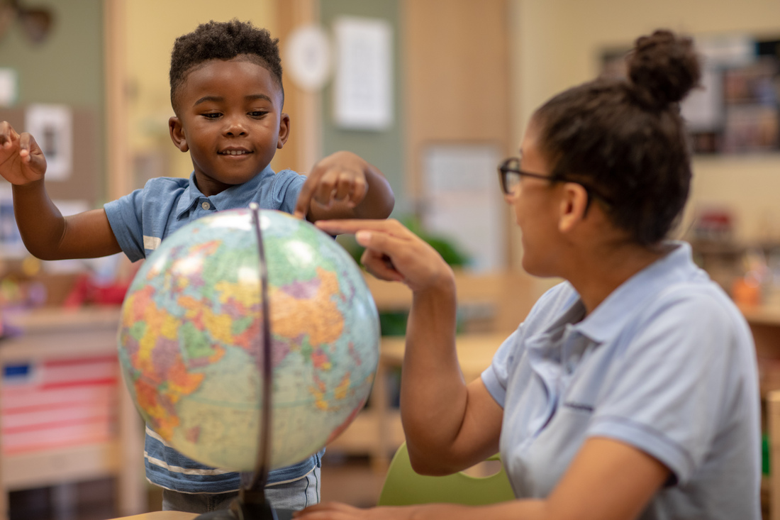 Adult helping a child explore a globe at a classroom table.