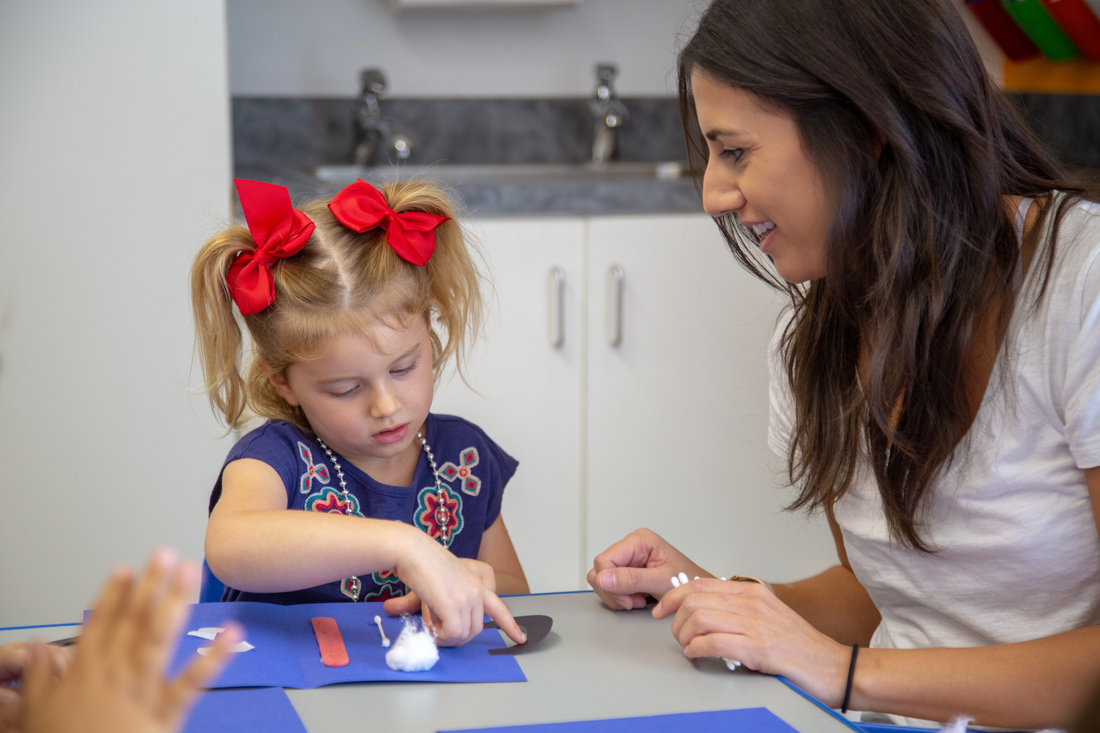 Child working on an art project with teacher at a table.