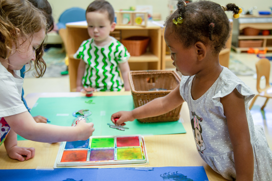 Toddlers painting with watercolors at a classroom table.