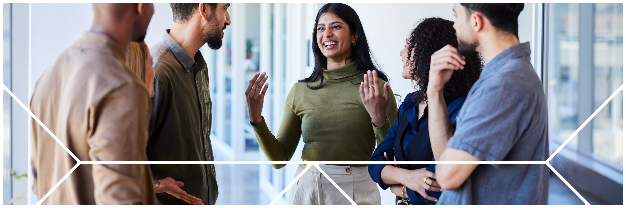 Five colleagues stand in a hallway, smiling and engaged in conversation. One woman gestures enthusiastically while others listen and interact. The image is framed by a white geometric design from Bon Secours Mercy Health branding.