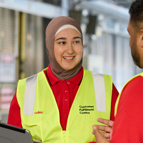 Coles team member wearing a high-visibility vest and holding a clipboard in a distribution centre, demonstrating safety, collaboration, and equal opportunity in the workplace.