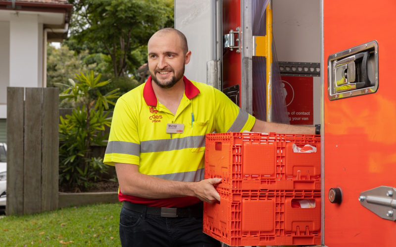 Coles Online team member carrying delivery crates beside a delivery van.