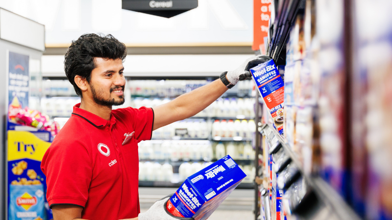 Young Coles team member replenishing products in a supermarket aisle