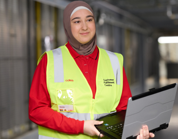Employee in a high-visibility vest using a laptop in a distribution centre.