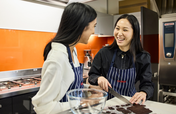 Two team member product testing inside a kitchen, with chopped chocolate on a bench.