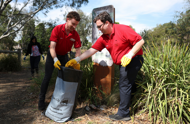 Team members wearing gloves collect litter into a bag along a bushland walking path.