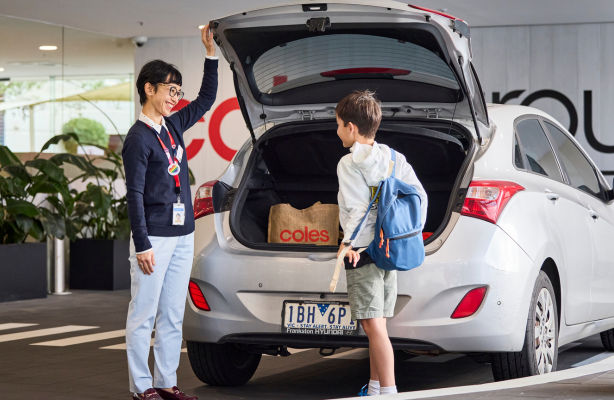 A team member assists a young person placing grocery bags into the open boot of a parked car.