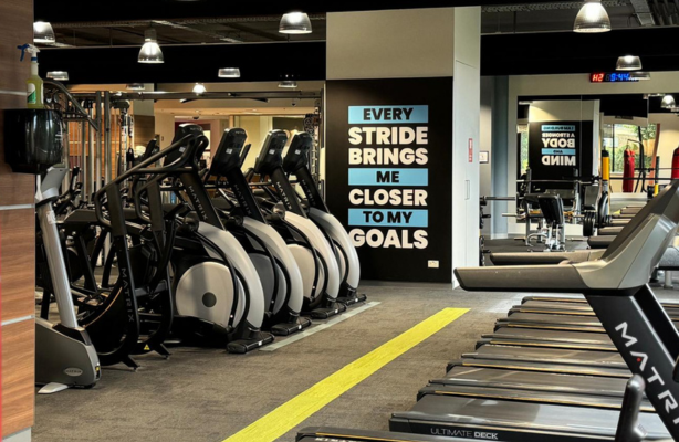 Indoor gym with rows of treadmills and cardio machines, and a wall sign reading “Every stride brings me closer to my goals.