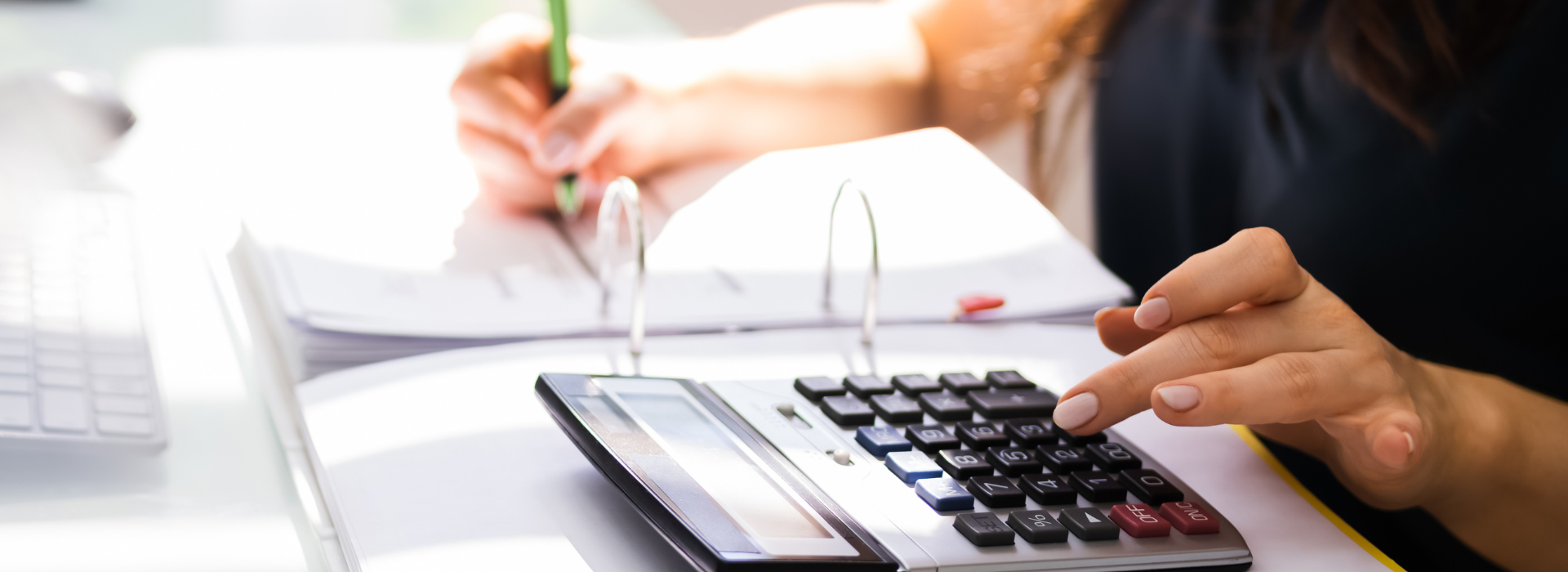 woman's hands using a calculator and making notes in ledger
