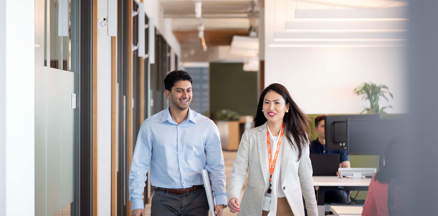 Two colleagues walk down a bright office corridor, one wearing a GSK orange lanyard.