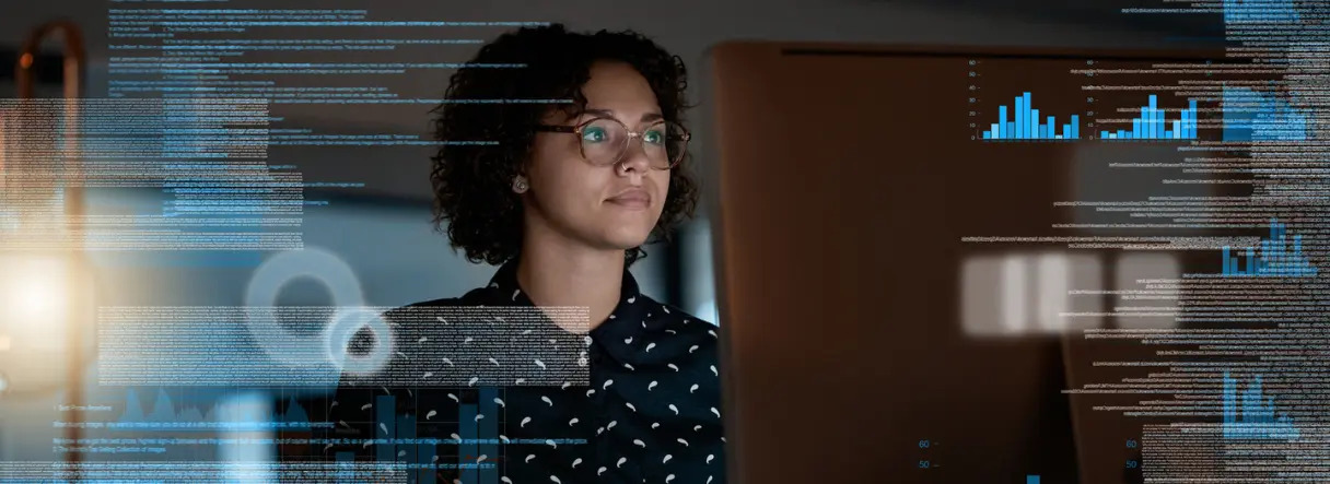 A person with curly hair and glasses looks at a computer monitor, with digital data, graphs, and code superimposed, suggesting data analysis or programming work.