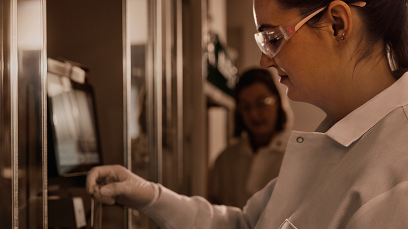 A woman in a lab coat and gloves operating equipment in a laboratory or industrial setting