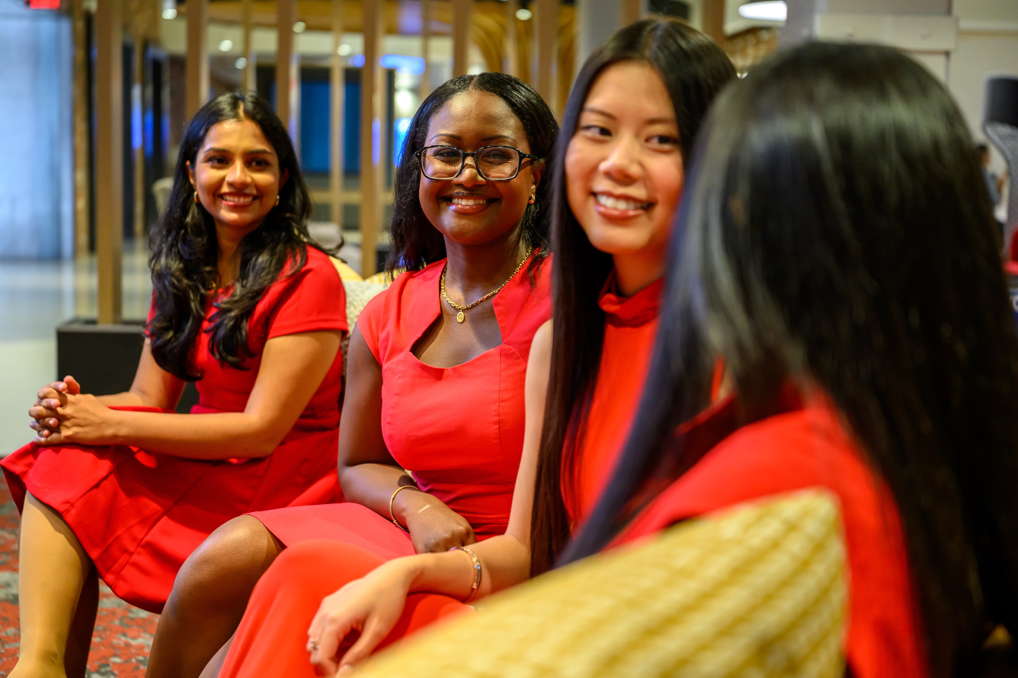 Four professionals seated together in a workplace lounge area, participating in a conversation during a networking or team-building event. The informal setting features modern furnishings and open gathering spaces designed for employee connection and collaboration.