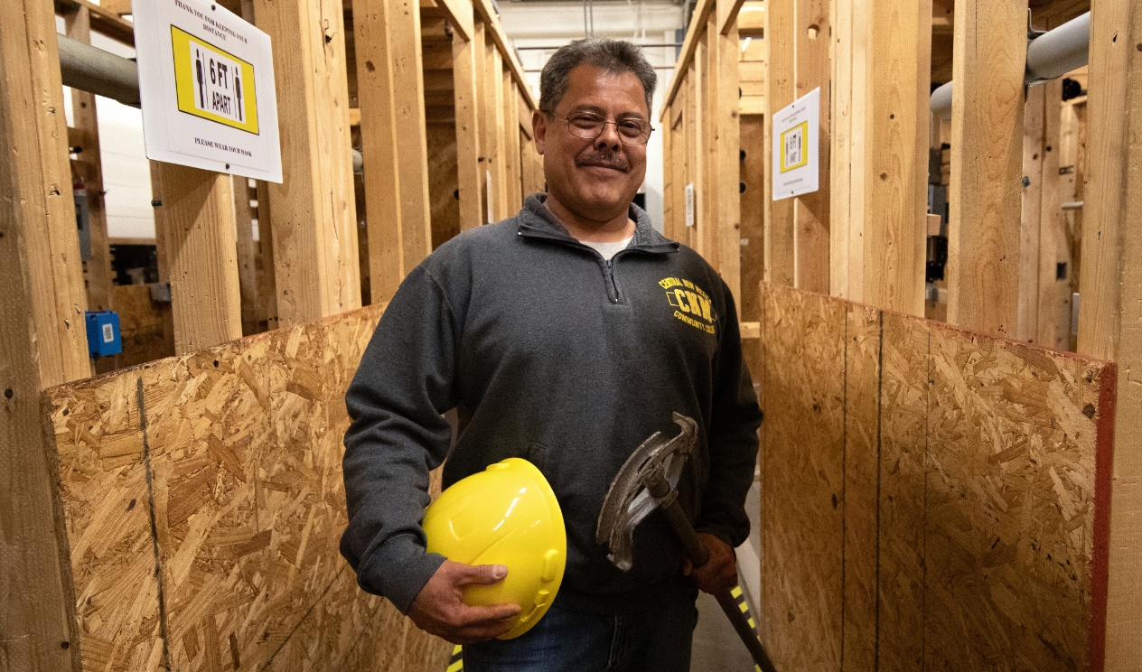 Instructor standing by framed walls holding electrical equipment