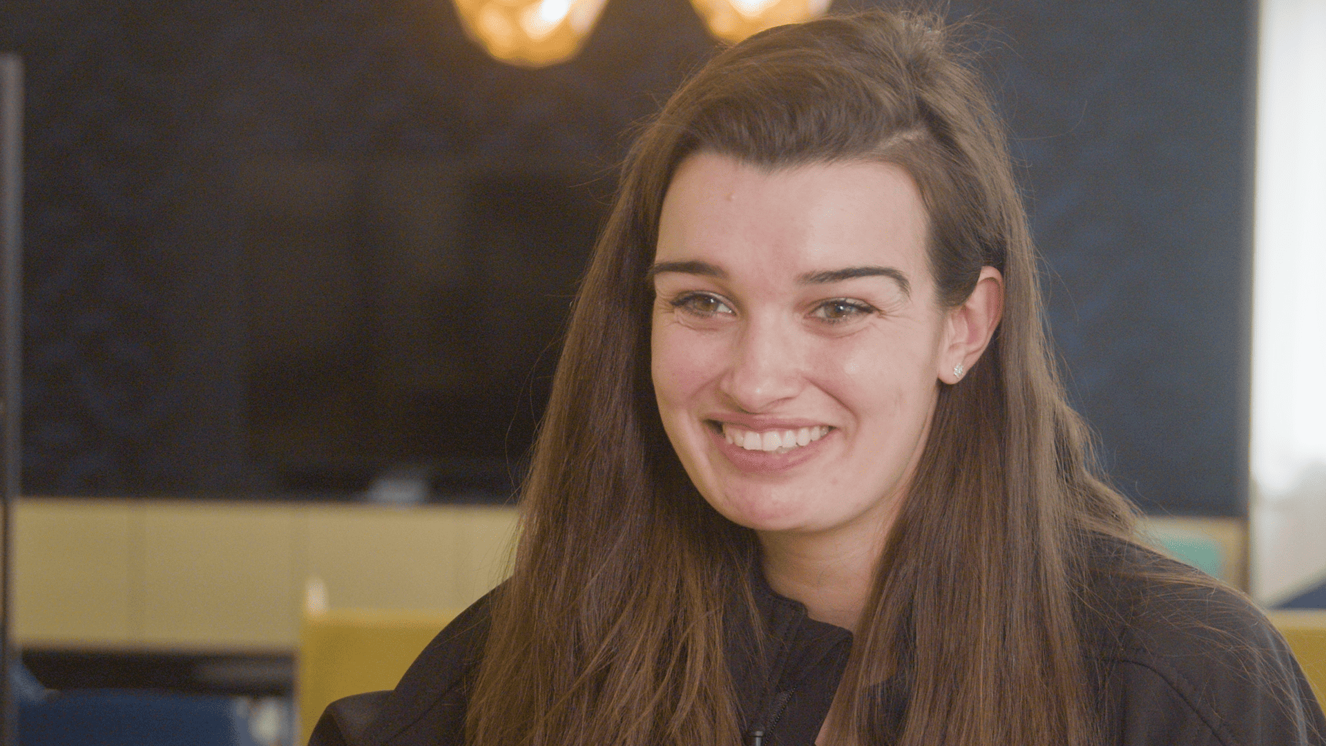 Alexia smiling during an interview about her work-study experience, with a warm, blurred office lounge in the background.