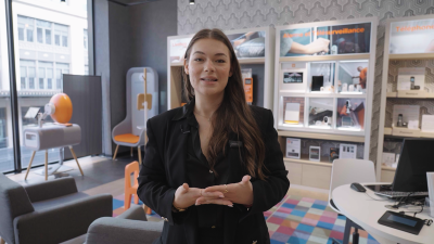 Christina speaking in a modern Orange Store showroom, surrounded by displays for home alarms and telephony services.