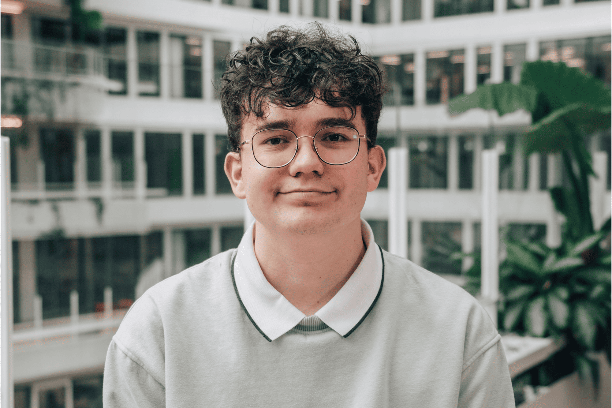 Nicolas, a work-study student wearing glasses, smiling in a high-tech corporate building courtyard.