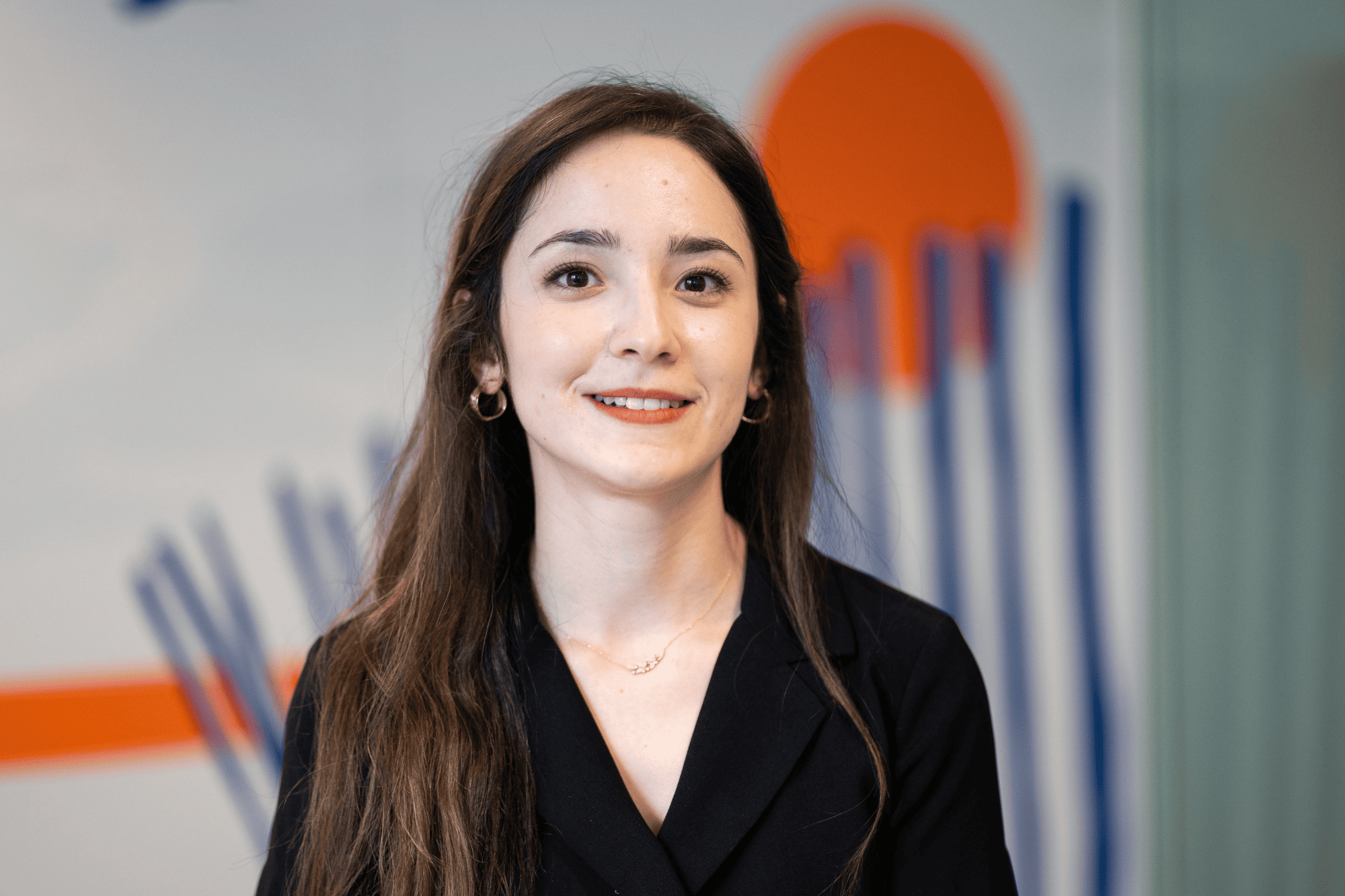 Professional portrait of Nour, a collaborator at Sofrecom, smiling in a modern office with orange and blue wall art.