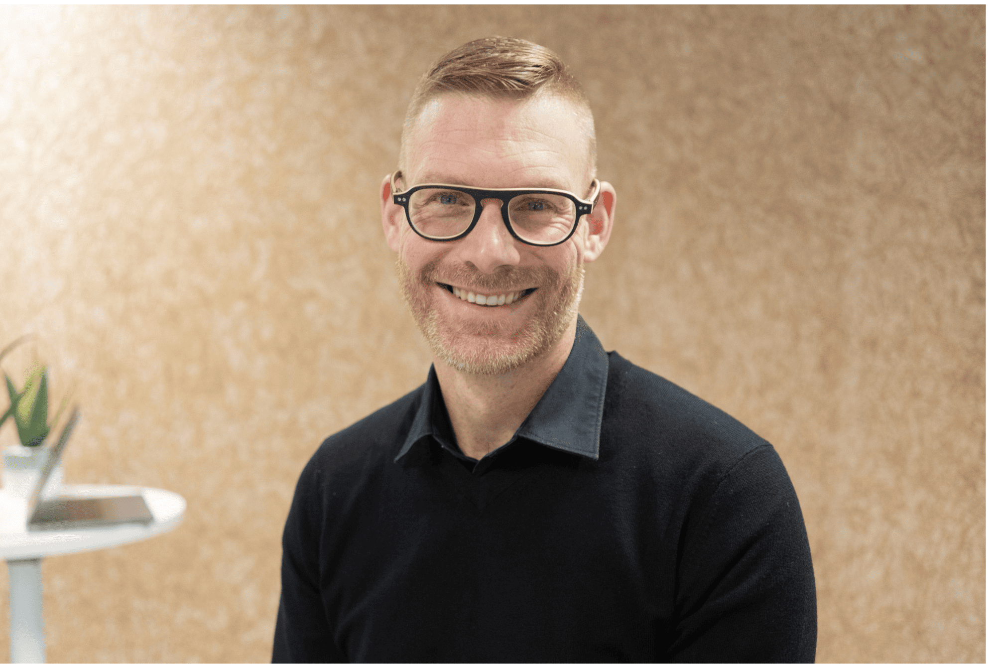 Professional portrait of Pierre-Yves, a Solution Integrator wearing glasses and a black sweater, smiling in a bright workspace.